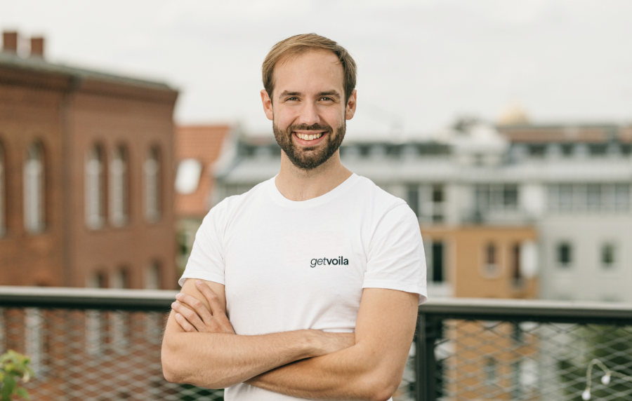 Ein lächelnder Mann in einem weißen T-Shirt steht auf einem Balkon und erhält ein Startup-Coaching.