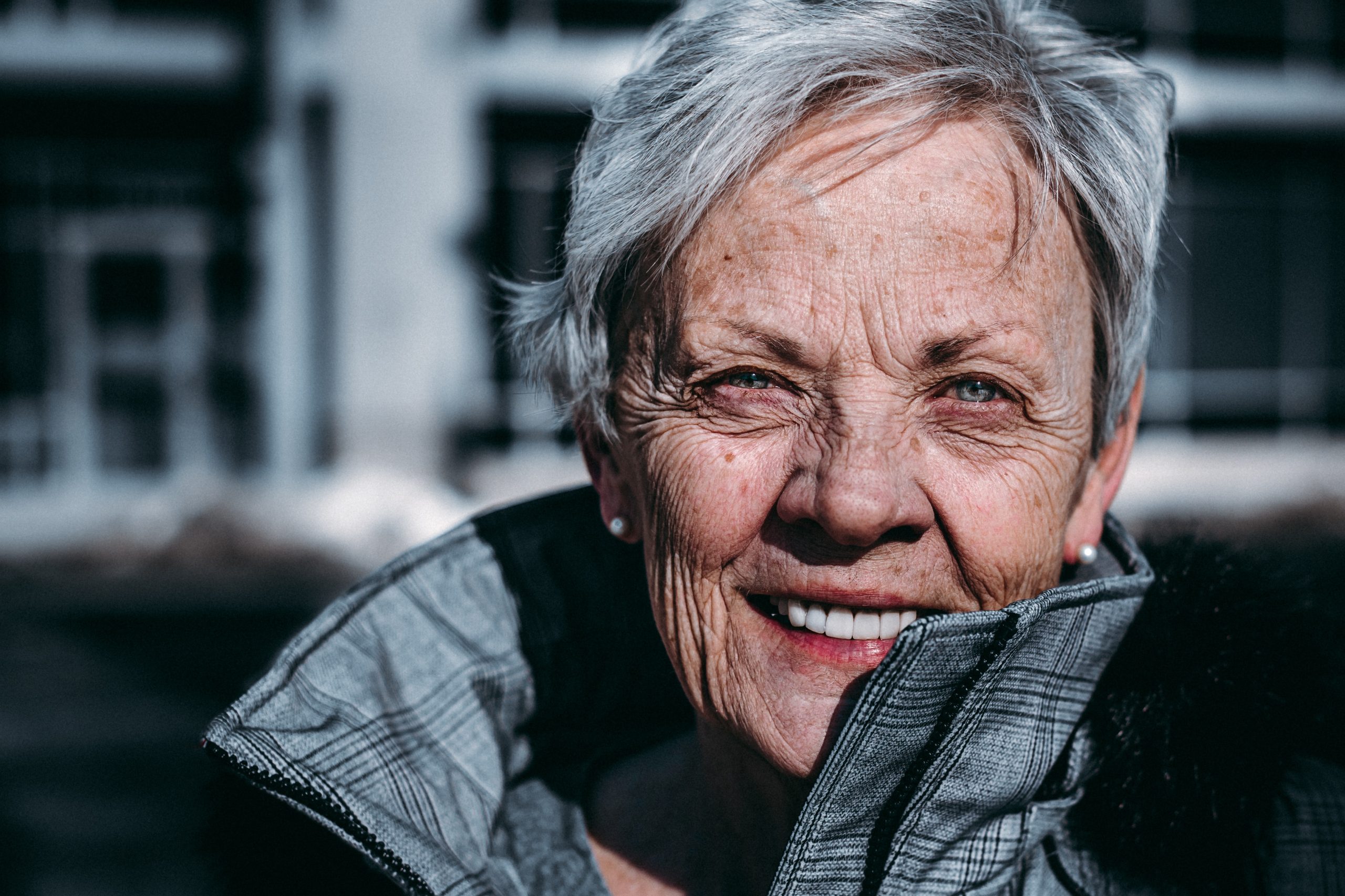Eine ältere Frau lächelt vor einem Gebäude und erhält ein Startup-Coaching.